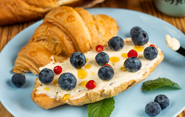 Croissant sandwich with cheese , arugula and berries. classic american breakfast. Fresh french croissant with fresh berries. blueberry and strawberry on cream cheese. Croissant and a cup with coffee 