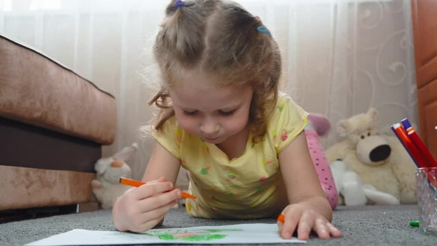 Pretty girl child, lying on the floor, drawing a child's drawing on the paper with floumats. Kids' leisure time, children's art. 4k footage