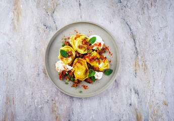 Traditional oriental manti dumplings with spicy minced meat and yogurt served as top view in a Nordic design plate with text free space