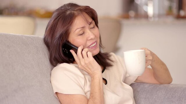 Attractive woman relaxing talking on mobile phone drinking coffee sitting in comfortable living room of leisure home