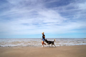 A beautiful girl runs with a husky dog ​​on the beach on a summer day.