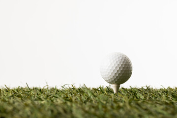 Close up of white golf ball on tee on grass with copy space on white background