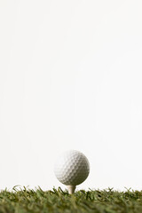 Close up of white golf ball on tee on grass with copy space on white background