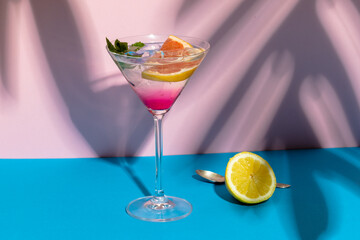 Glass of cocktail over beige and pink surface with shadows