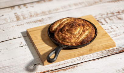 Cinnamon bun in black metal pan on the wooden table.