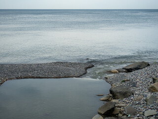 The place where a small river flows into the sea. Winter on the Black Sea. Empty coast. Beach of boulders and small pebbles.