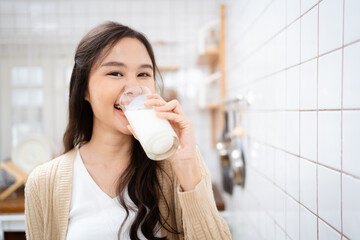 Beautiful happy Asian woman drinking a milk in morning in kitchen and smiling to camera.