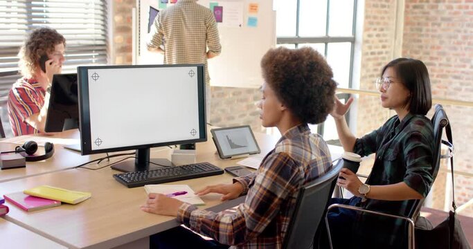 Two happy diverse businesswomen using computer in casual office, copy space on screen, slow motion