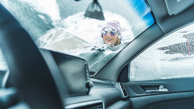 Smiling woman in sunglasses scraping snow off a front car window. High quality photo