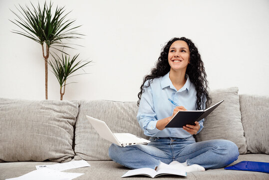 Beautiful student of Arab appearance thought about the study plan and management. Girl sits on a sofa and looks into the distance holding a notebook and a pen in her hands
