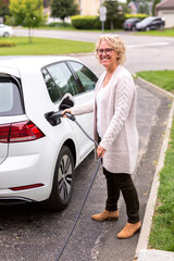 Une femme dans la quarantaine installe son câble d'alimentation sur ta voiture électrique dans son allée de maison.