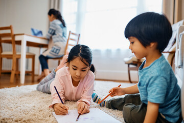 Small Asian kids coloring on paper at home.