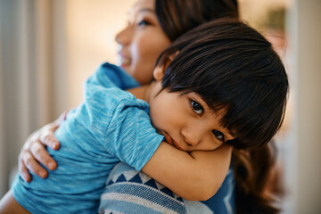 Sad Asian boy being consoled by his mother at home.