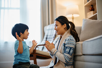 Happy Asian kid and his mother have fun while playing clapping game at home.