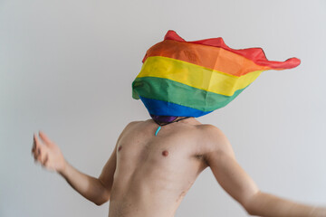 Young latin gay queer man screaming while lgbt flag covers his face on a white background.