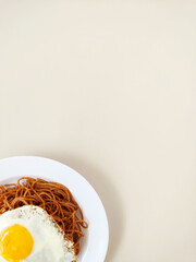 Partial view of top of a Plate with wholemeal spaghetti pasta, fried egg on the top and pieces of garlic and blank space to text. Ready  Template.