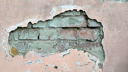 The texture of a wall with crumbled plaster through which bricks can be seen. Background