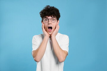 Portrait of shocked teenage boy wearing glasses on light blue background © New Africa