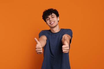 Handsome young man showing thumbs up on orange background
