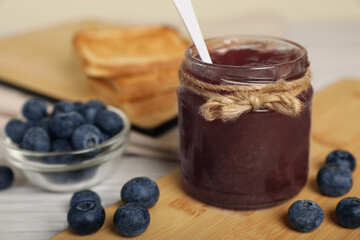 Jar of delicious blueberry jam and fresh berries on white wooden table, closeup. Space for text