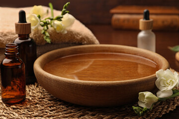 Bowl of water, bottles with essential oil and beautiful roses on table. Aromatherapy treatment