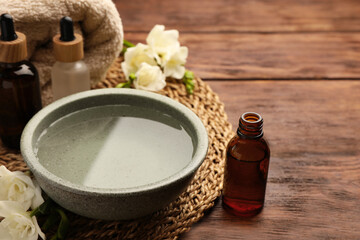 Bowl of essential oil and beautiful flowers on wooden table, space for text. Aromatherapy treatment