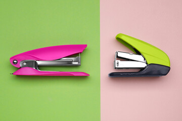 New bright staplers on color background, flat lay. School stationery