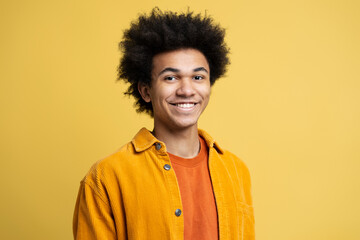 Portrait of confident smiling African American man with curly hair wearing stylish casual clothing isolated on yellow background. Happy successful student looking at camera. Education concept