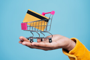 Hand holding shopping trolley with credit card isolated on blue background, selective focus....