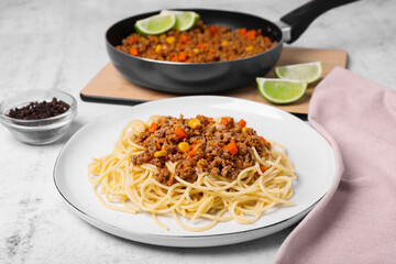 Tasty dish with fried minced meat, spaghetti, carrot and corn on served white textured table