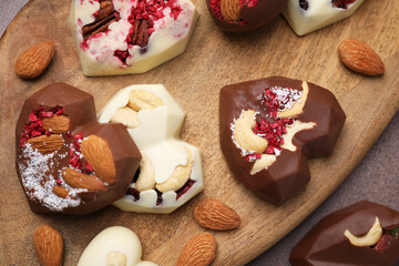 Tasty chocolate heart shaped candies with nuts on brown textured table, flat lay