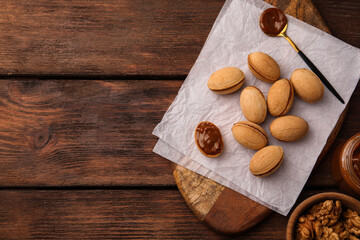 Delicious nut shaped cookies with boiled condensed milk on wooden table, flat lay. Space for text