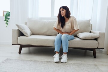 Obraz premium Woman sitting on sofa at home back and stomach pain during menstruation, women's day, women's health problems, suspected appendicitis