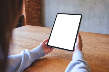 Mockup image of a woman holding digital tablet with blank white desktop screen on wooden table