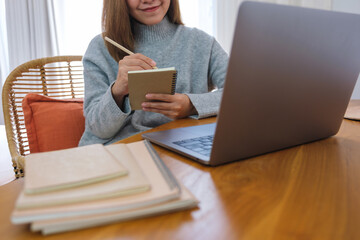 Closeup image of a young woman writing on notebook while working or study on laptop computer at home