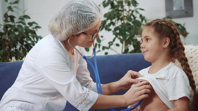 Woman Doctor Listens To A Small Kid Child Treats. Medicine Health Care Covid 19 Child Care Pandemic Coronavirus Concept. Woman Doctor Treats A Little Girl. Daughter At The Doctors Appointment