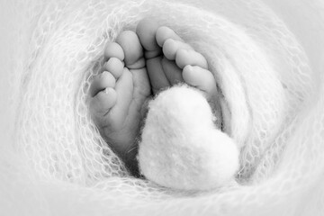 Knitted heart in the legs of a baby. Soft feet of a new born in a wool blanket. 