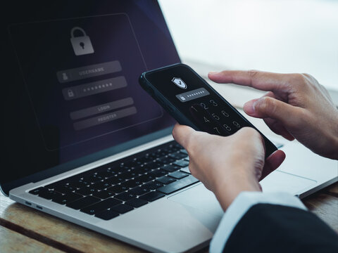 Two steps authentication (2FA) concept. Shield icon and password code showing on smart phone screen while businessperson login on laptop computer, Identity verification, cybersecurity technology.
