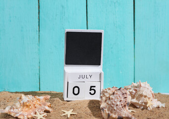 Beach holiday composition with sand, sea souvenirs and wooden block calendar with date july 05....