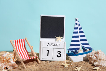 Beach holiday composition with sand, seashells, sailboat, deck chair and wooden block calendar with date august 13. Vacation, summertime, creative travel still life
