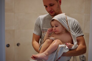 Obraz na płótnie Canvas Little toddler in towel after bath holding by his father