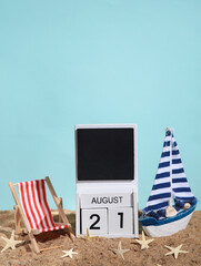 Beach holiday composition with sand, seashells, sailboat, deck chair and wooden block calendar with date august 21. Vacation, summertime, creative travel still life