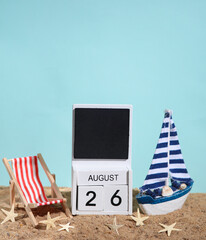 Beach holiday composition with sand, seashells, sailboat, deck chair and wooden block calendar with date august 26. Vacation, summertime, creative travel still life