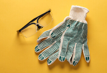 Safety goggles and working gloves on yellow background. Top view. Copy space