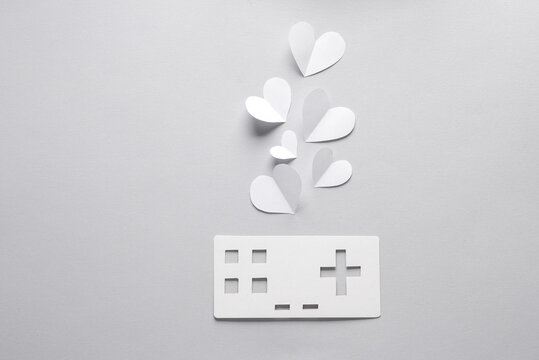 Paper retro gamepad icon with hearts on gray background. Paper art