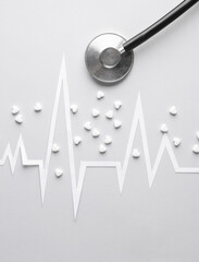 Diagnosis of heart diseases. Paper-cut heart rhythm cardiogram with heart-shaped pills and stethoscope on gray background