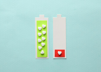 Paper cut full and low battery with heart shaped pills on blue background