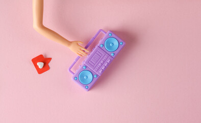 Doll's hand holding Miniature boombox tape recorder with Social media like on pink background....