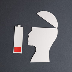 Depression. Silhouette of head cut out of paper and battery with low level of charge on a gray...