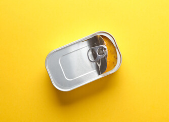 Open tin can with food on yellow background. Top view